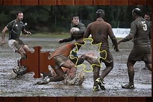 Rugbyspillere dekket av gjørme spiller på en sølete bane, med et manglende puslespillbrikkeeffekt over bildet