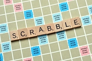 Trehvite bokstavbrikker staver ordet SCRABBLE på et rutete brett med fargerike bonusfelter