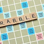 Trehvite bokstavbrikker staver ordet SCRABBLE på et rutete brett med fargerike bonusfelter